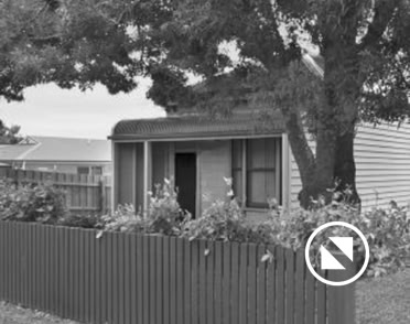 A small house with a porch, surrounded by a wooden fence and trees.